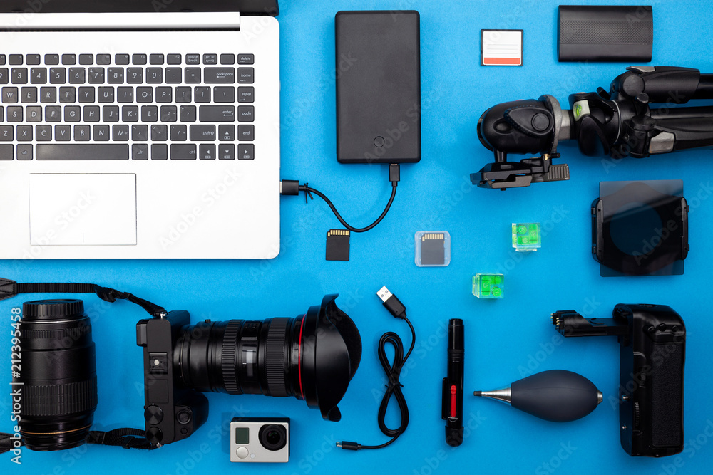 Digital camera with lenses and equipment of the professional photographer on blue paper background.