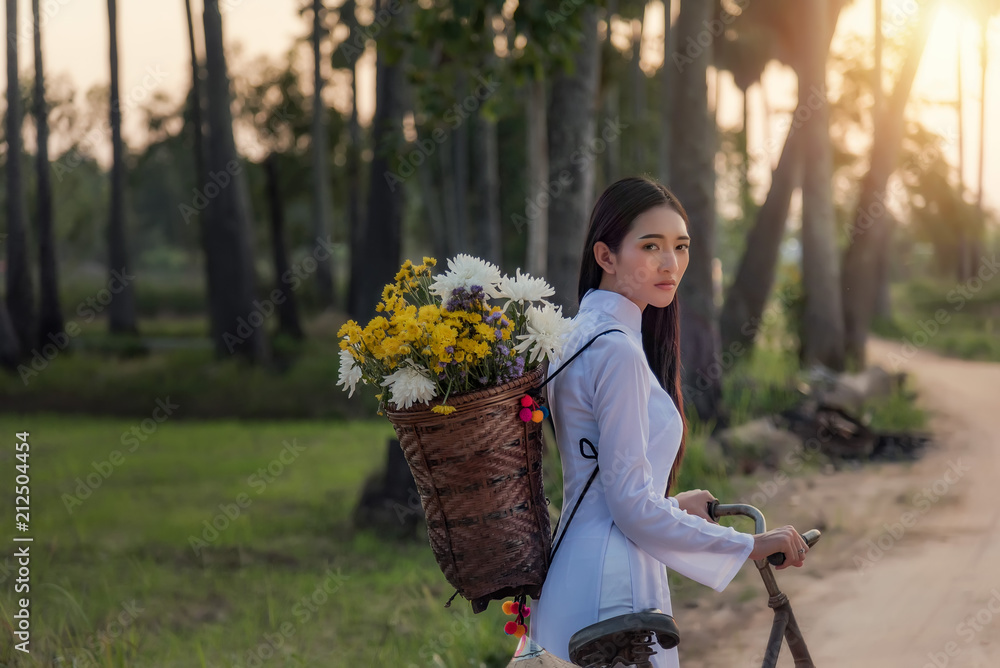 穿着越南服装的女子敖黛骑着自行车在乡村的一条路上