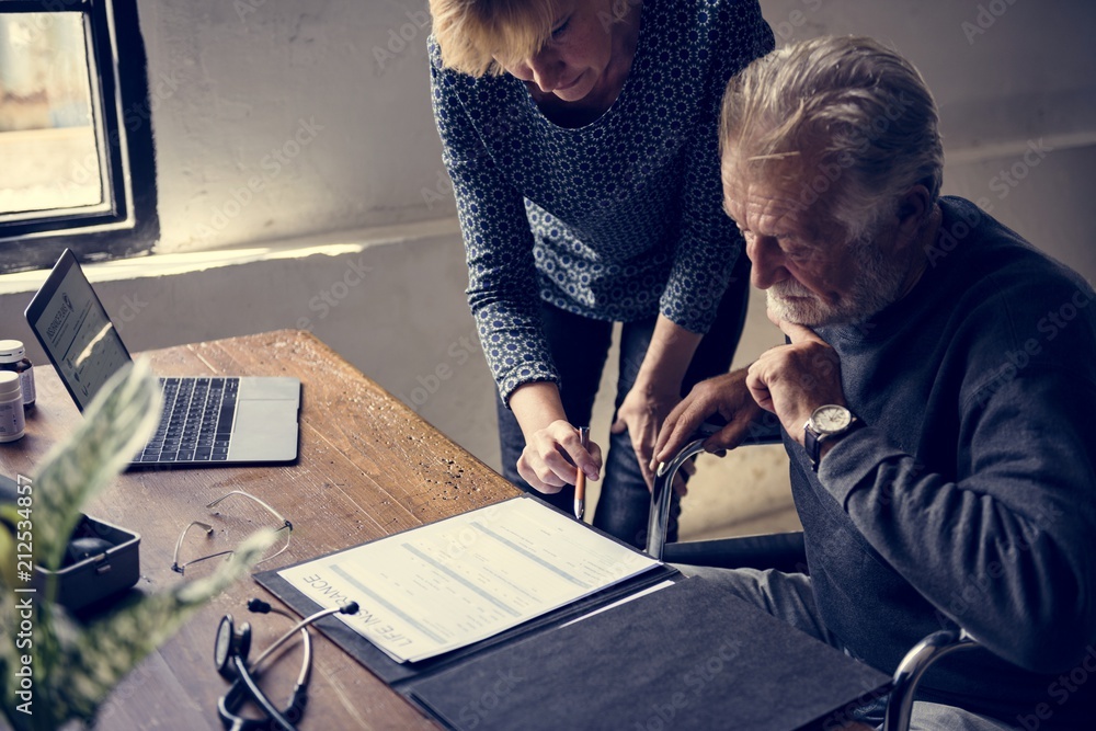 Side view of elderly man sitting on wheelchair looking at life insurance contract form