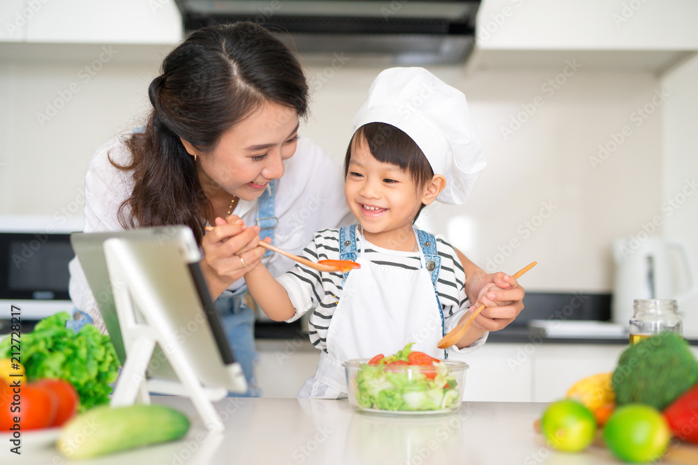 母亲和女儿在厨房准备午餐，一起享受。