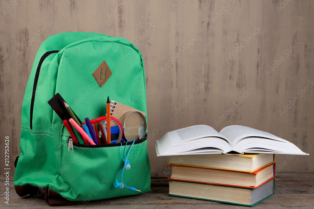 Education concept - school backpack with books and other supplies on the desk