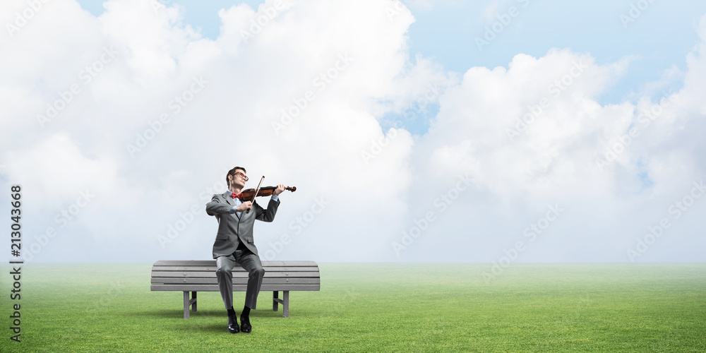 Handsome businessman in park on wooden bench play his melody