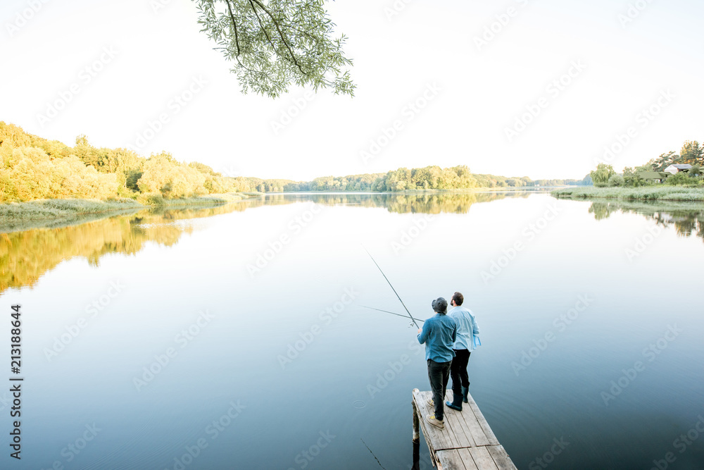 Landscape view on the beautiful lake with two male friends fishing together standing on the wooden p