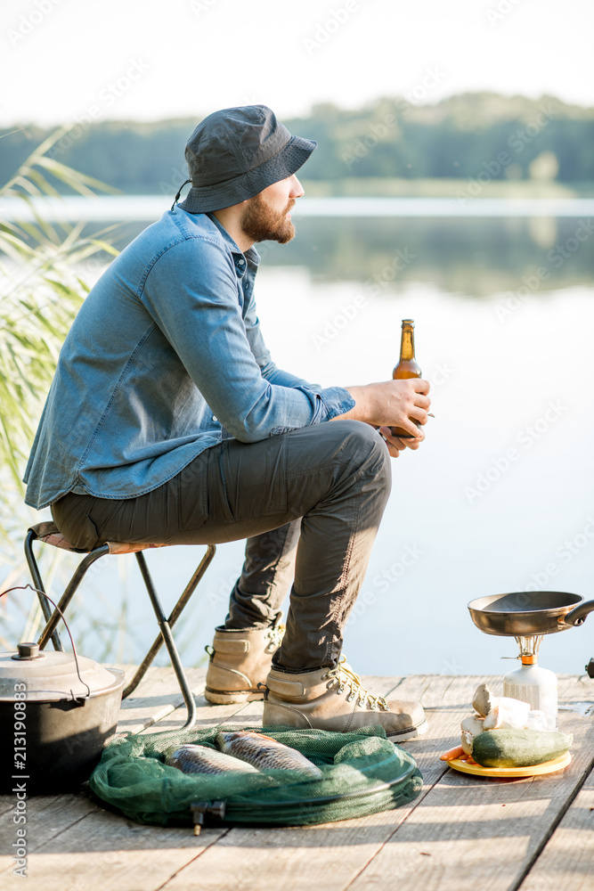 英俊男子在湖边码头钓鱼时独自坐着喝啤酒放松