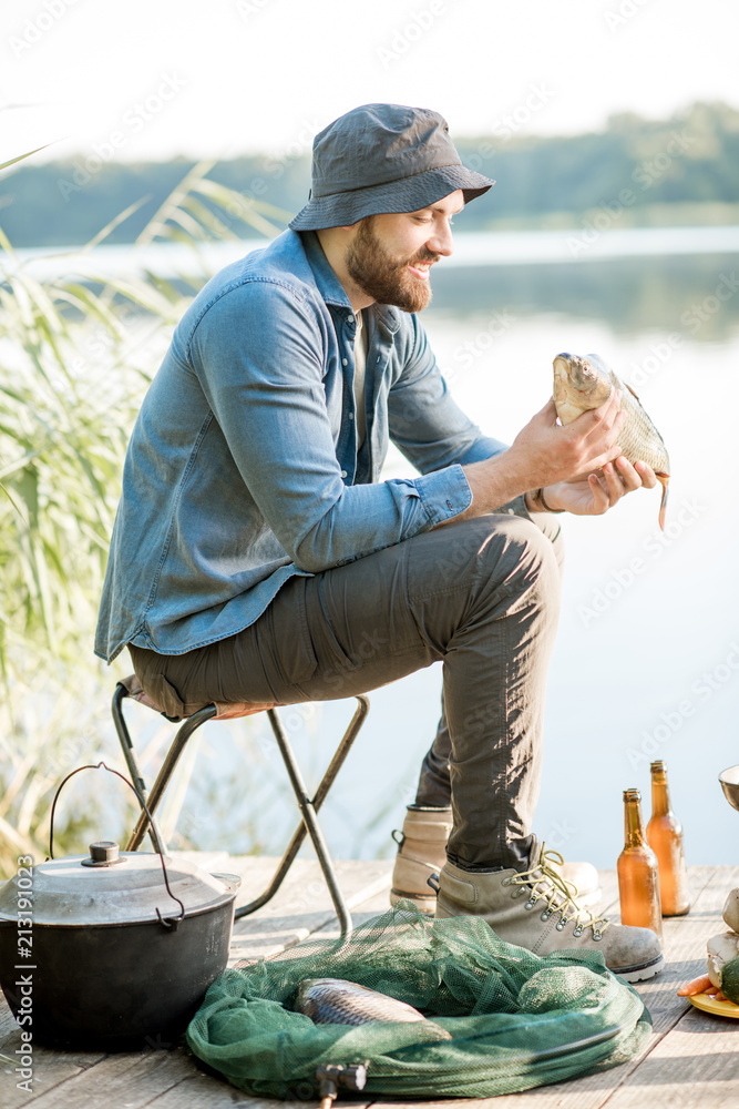 Happy fisherman holding caught fish ready to cook sitting during the fishing process near the lake