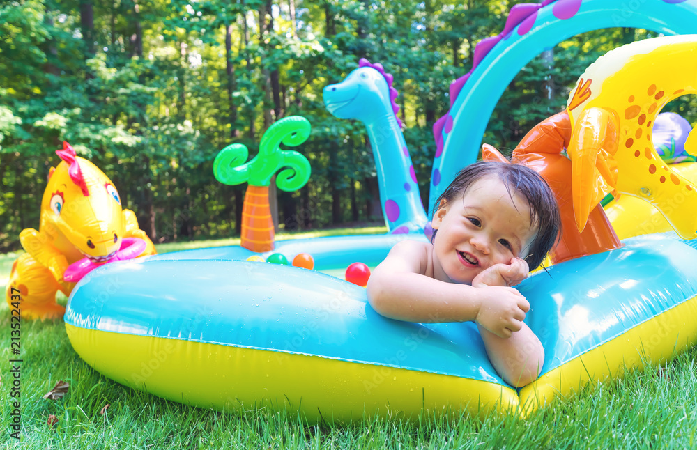 Happy toddler boy playing in his backyard pool