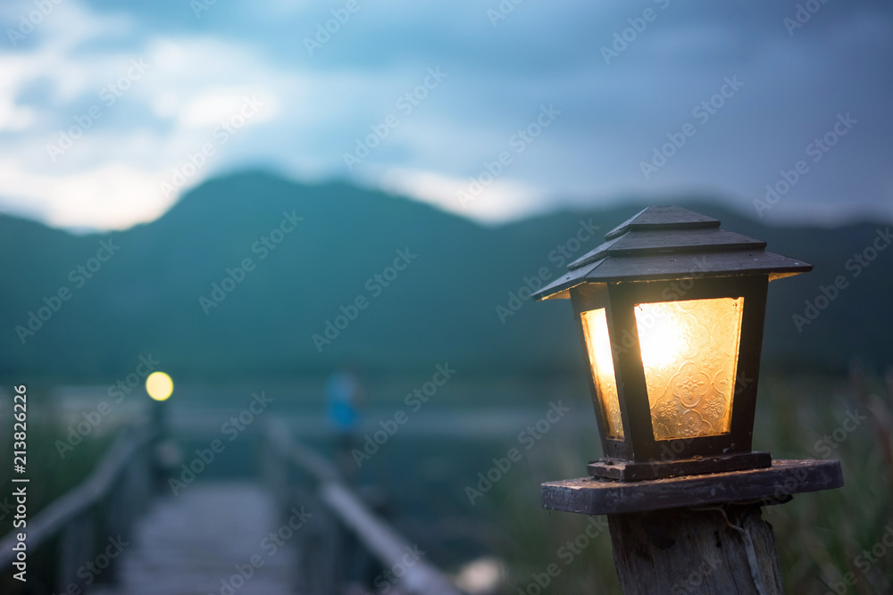 Orange light from Old lamp stand with man and mountain background at morning time.