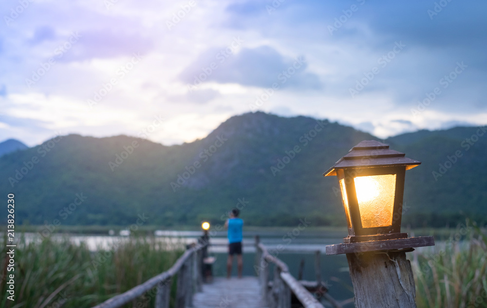 Orange light from Old lamp stand with man and mountain background at morning time.