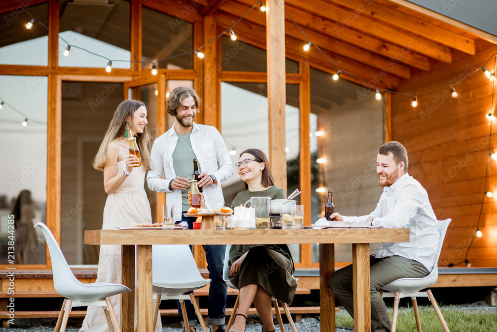 Young friends having fun during the dinner on the backyard of the modern wooden country house outdoo