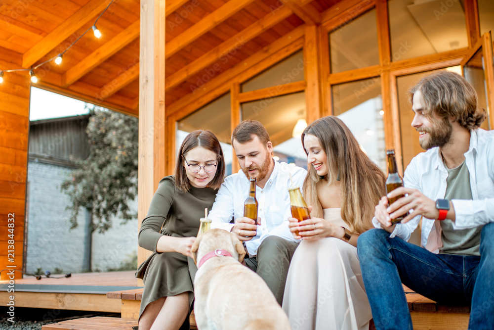 Young friends enjoying evening time sitting together with dog on the terrace of the modern wooden ho