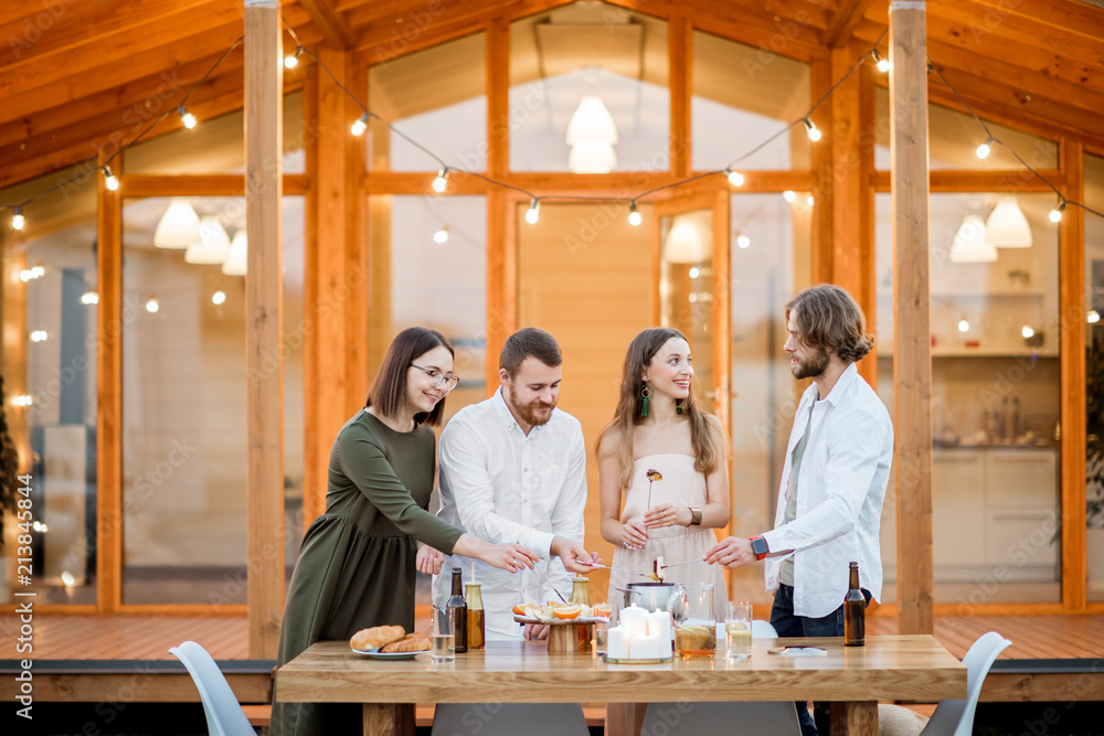 Four friends enjoying evening time having a dinner on the backyard of the modern country house outdo