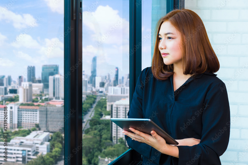 Attractive yound businesswoman holding computer tablet and deep in thought looking out her office la