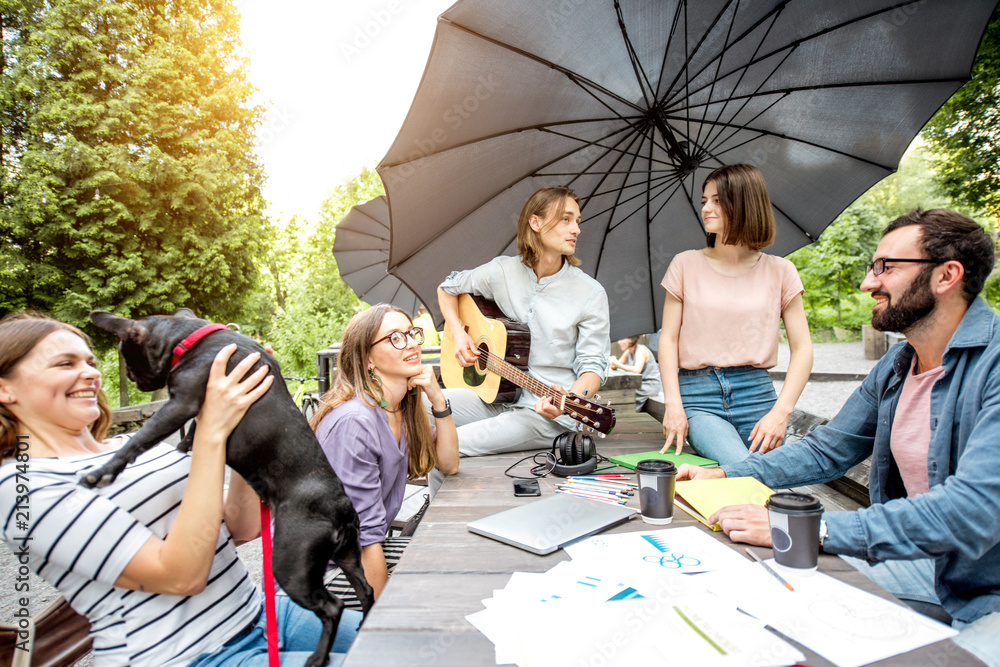 Young friends having fun playing guitar and playing wiwth dog outdoors in the park