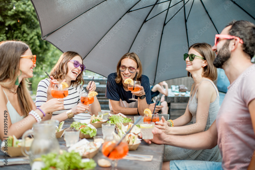 Young friends having fun together with snacks and drinks during the evening light outdoors in the pa