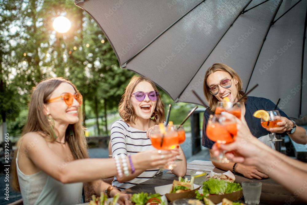 Young friends having fun together clinking glasses during the festive lunch outdoors in the park caf