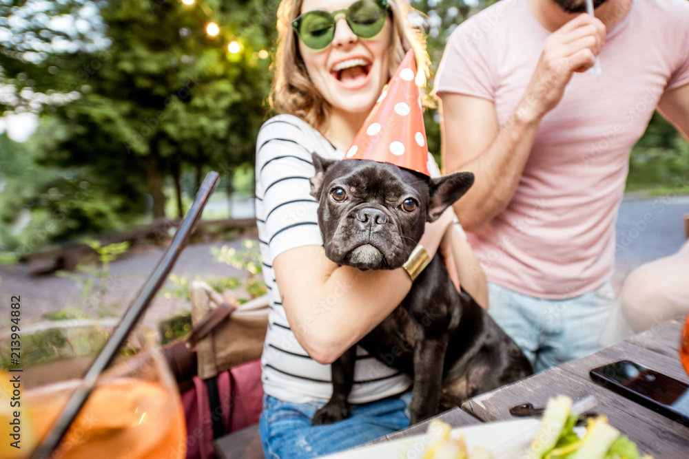 快乐的女人和法国斗牛犬晚上在户外与朋友庆祝生日