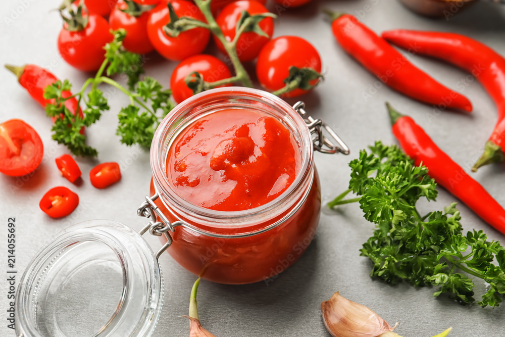 Jar of delicious tomato sauce on grey table