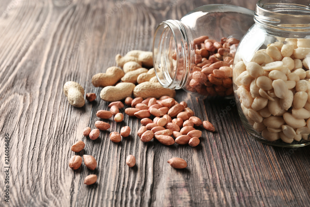 Glass jars with peanuts on wooden table