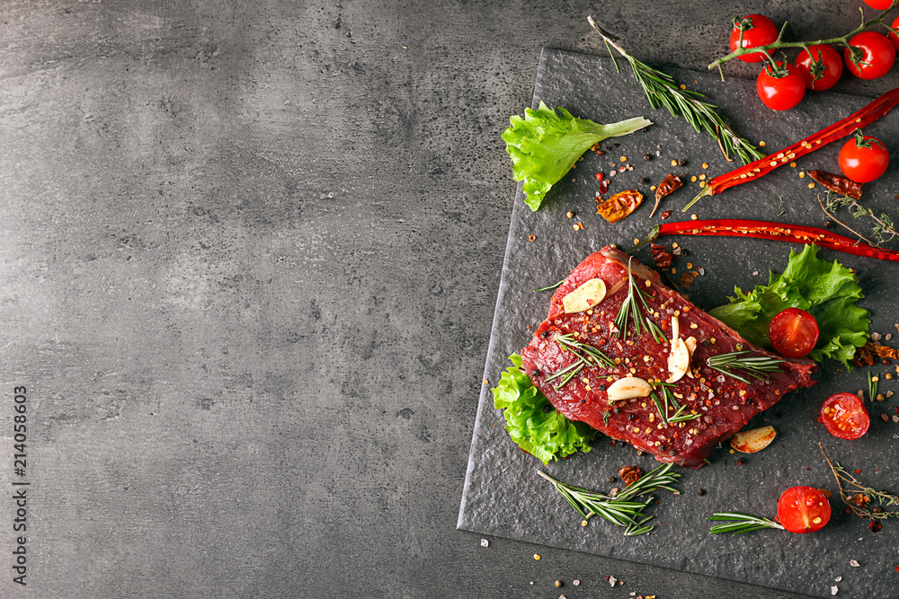 Slate plate with raw meat and vegetables on grey background, top view