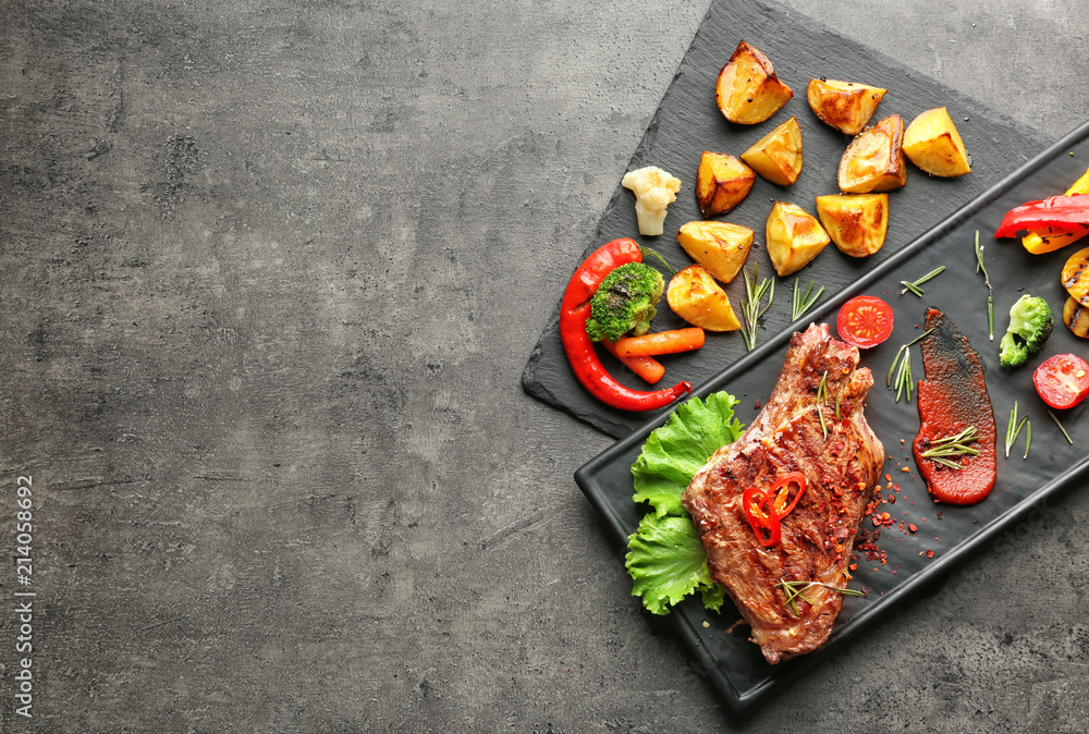 Plates with tasty meat and vegetable garnish on grey background, top view