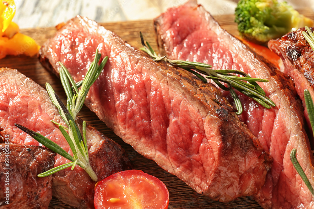 Wooden board with meat and vegetable garnish, closeup