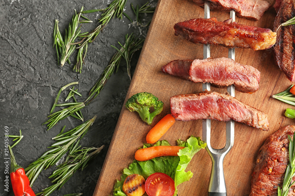 Wooden board with meat and vegetable garnish on grey background, top view