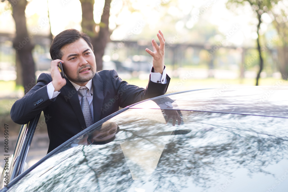 Handsome businessman in angry face using a mobile phone lerning on car