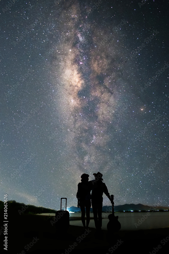 情侣旅行者站在湖边，看着夜晚天空中的银河和星星。silhouett