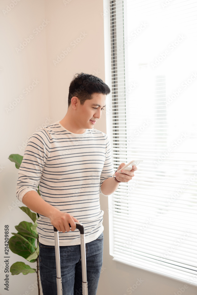 Happy asian man traveler standing with suitcase. and mobile phone in hotel