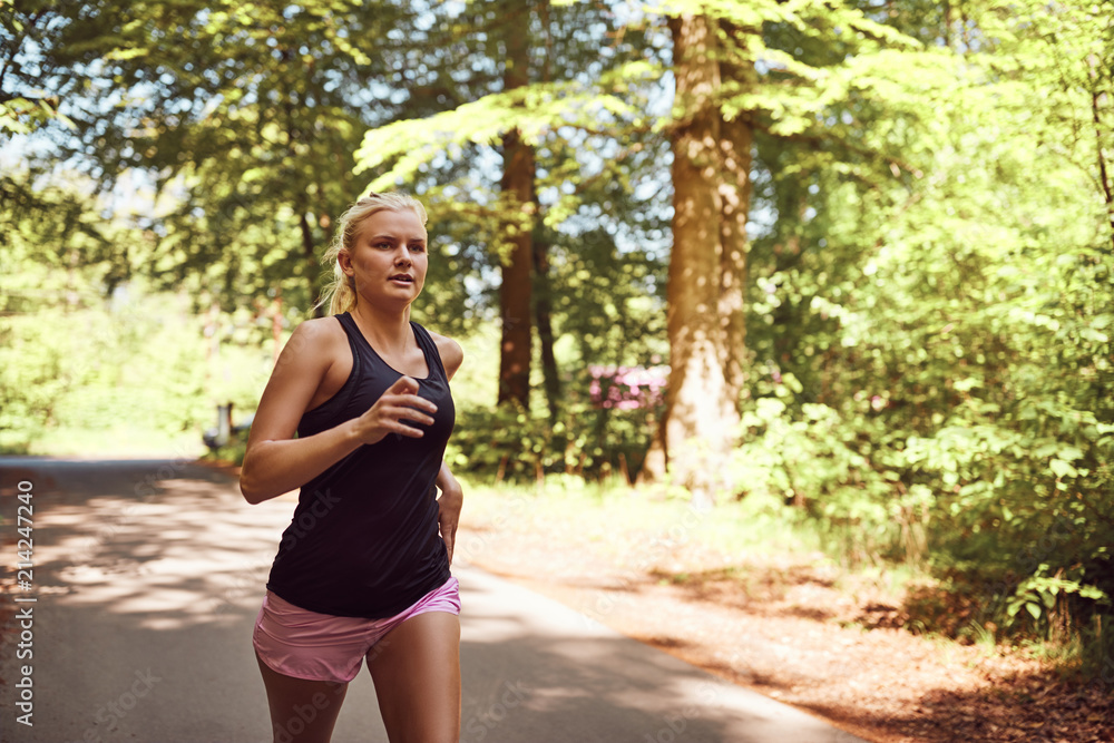 Fit young blonde woman jogging alone along a forest path