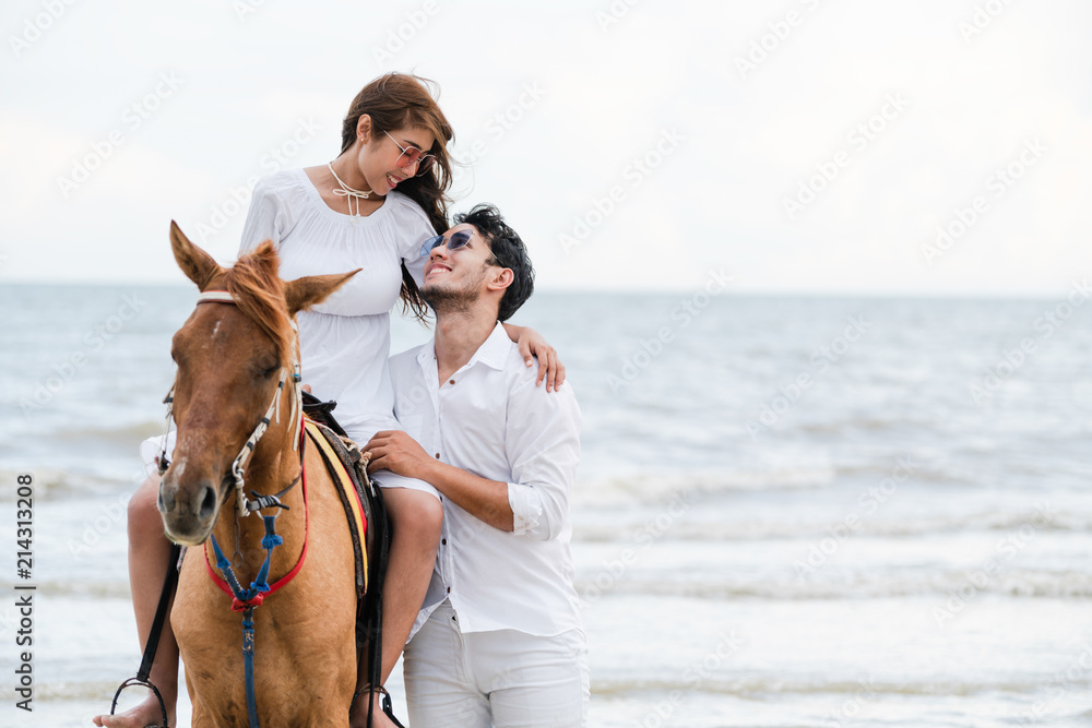 一对年轻夫妇在热带海滩上骑马。