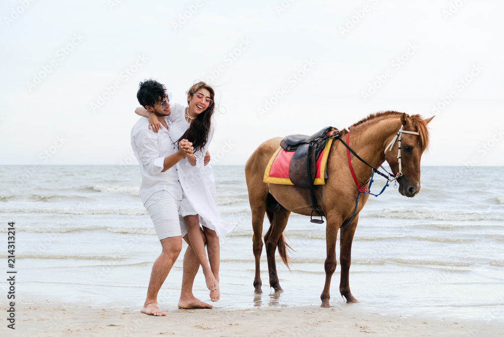 一对年轻夫妇在热带海滩上骑马。