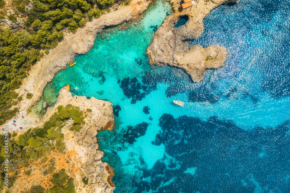 Aerial view of transparent sea with blue water, sandy beach, rocks, green trees, yachts and boats in