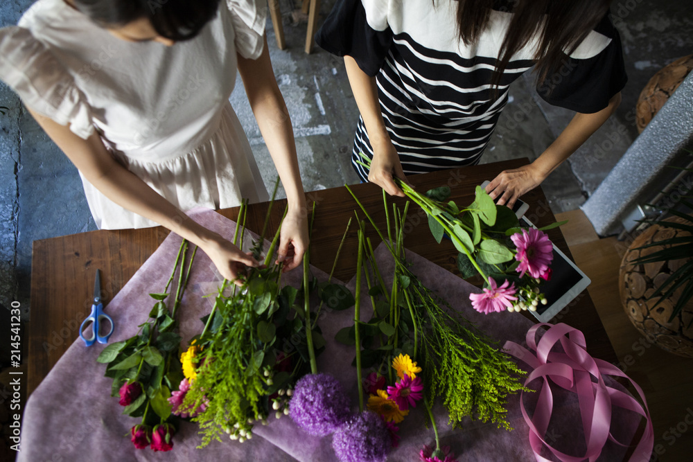 机に広がる色とりどりの花を切り揃え、花束を作る女性二人