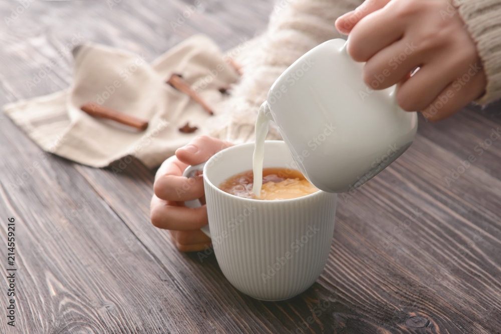 女人把牛奶倒进桌子上的一杯茶里