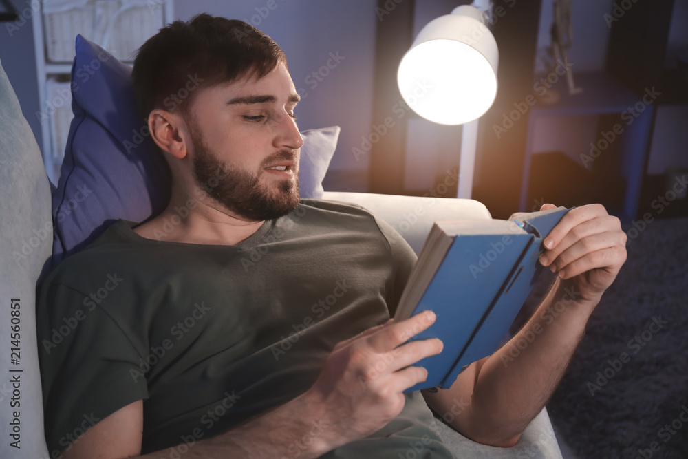 Young man reading book in evening at home