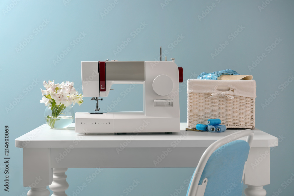 Table with modern sewing machine on color background