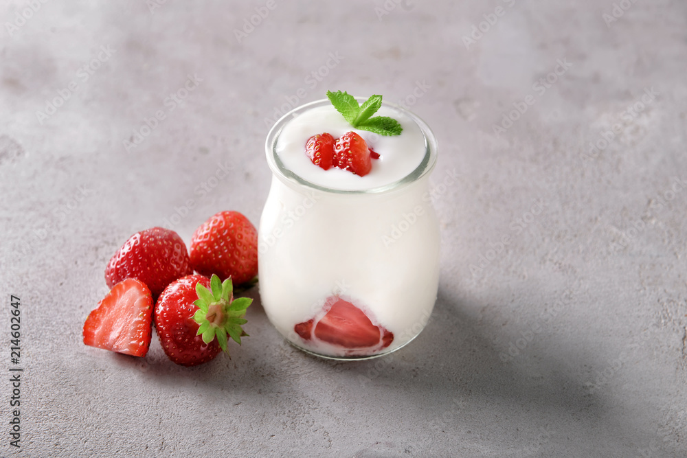 Glass jar with yogurt and strawberries on grey textured background