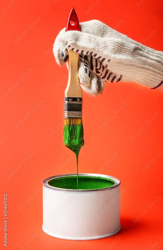 Worker holding brush dipped in paint on color background