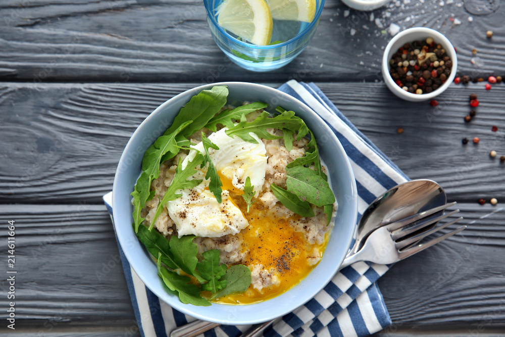 Bowl with delicious oatmeal, herbs and egg on wooden table