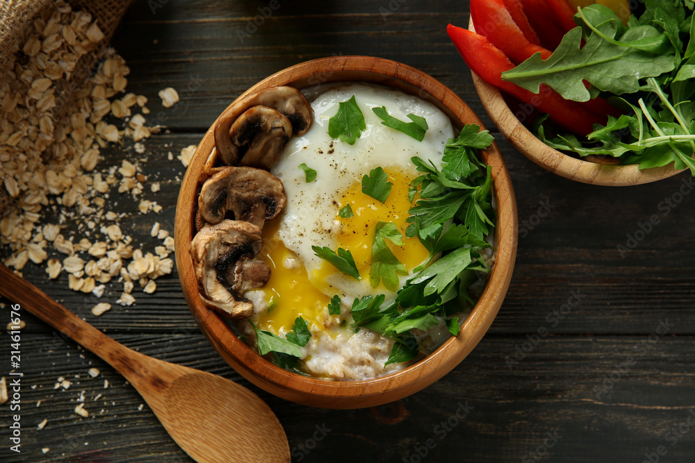 Bowl with delicious oatmeal, herbs and egg on wooden table