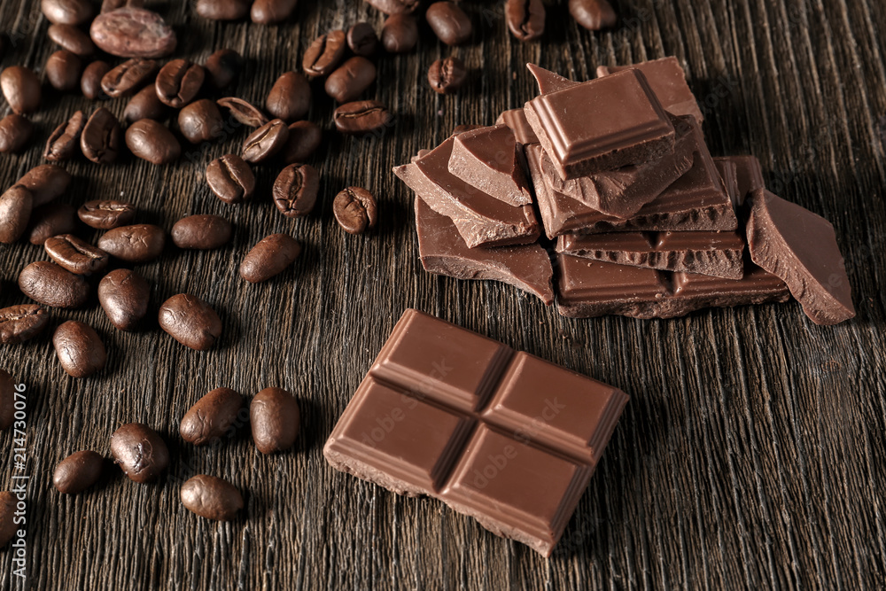 Pieces of tasty milk chocolate and coffee beans on wooden background