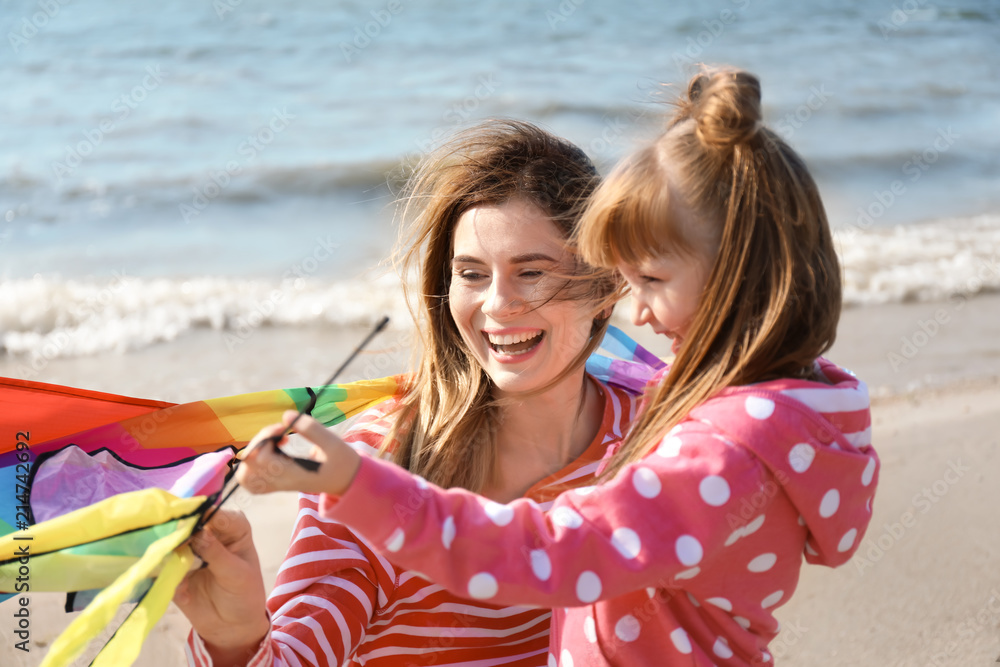 Little girl with mother flying kite near river