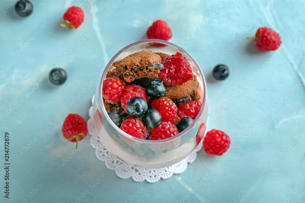 Glass with tasty raspberry dessert on color table