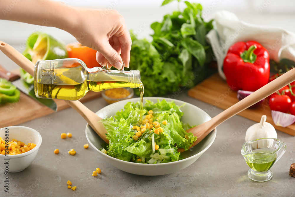 Woman adding olive oil to fresh vegetable salad on table, closeup