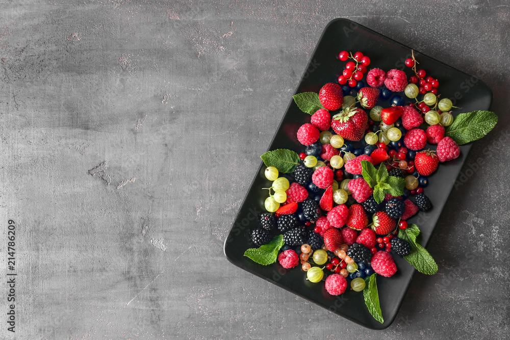 Plate with delicious ripe berries on grey textured background