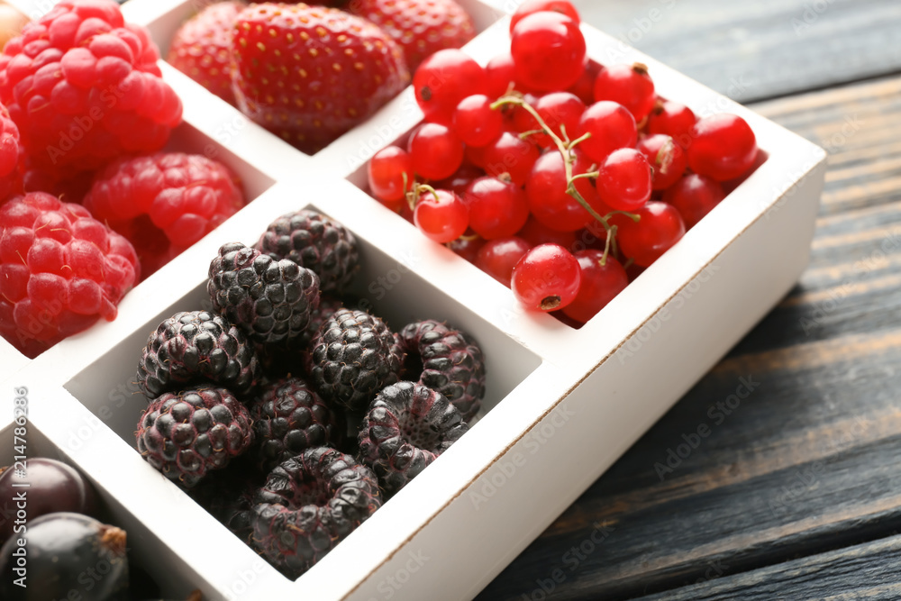 Partitioned box with delicious ripe berries on wooden background