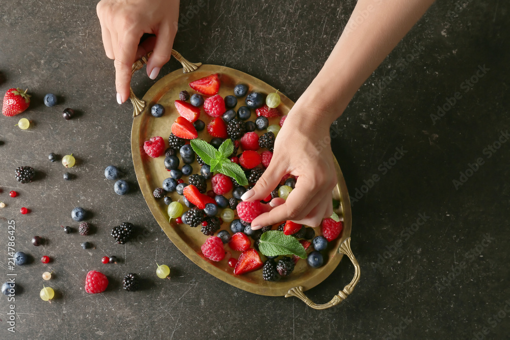 Woman taking fresh raspberry from tray with ripe berries on dark background