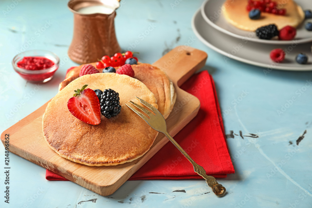 Board with tasty pancakes and berries on light table