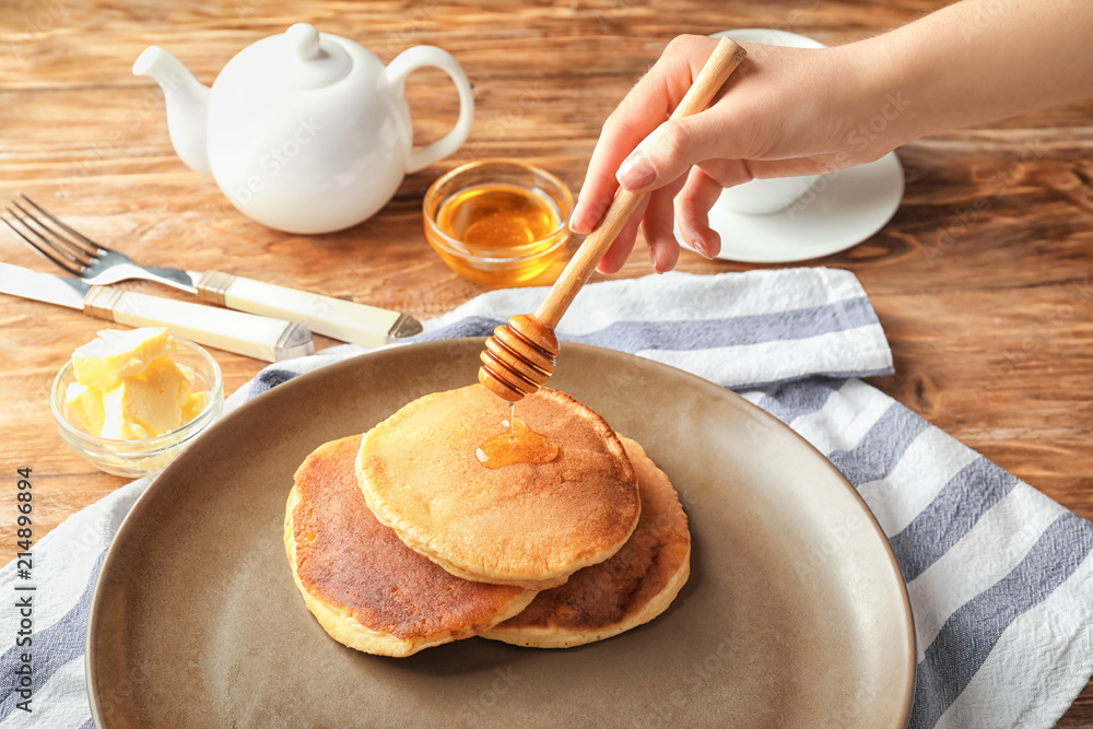 Woman pouring honey onto tasty pancakes